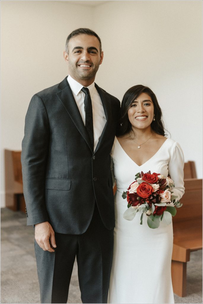 wedding couple embraces and smiles in courthouse wedding in maryland with red and pink bouquet