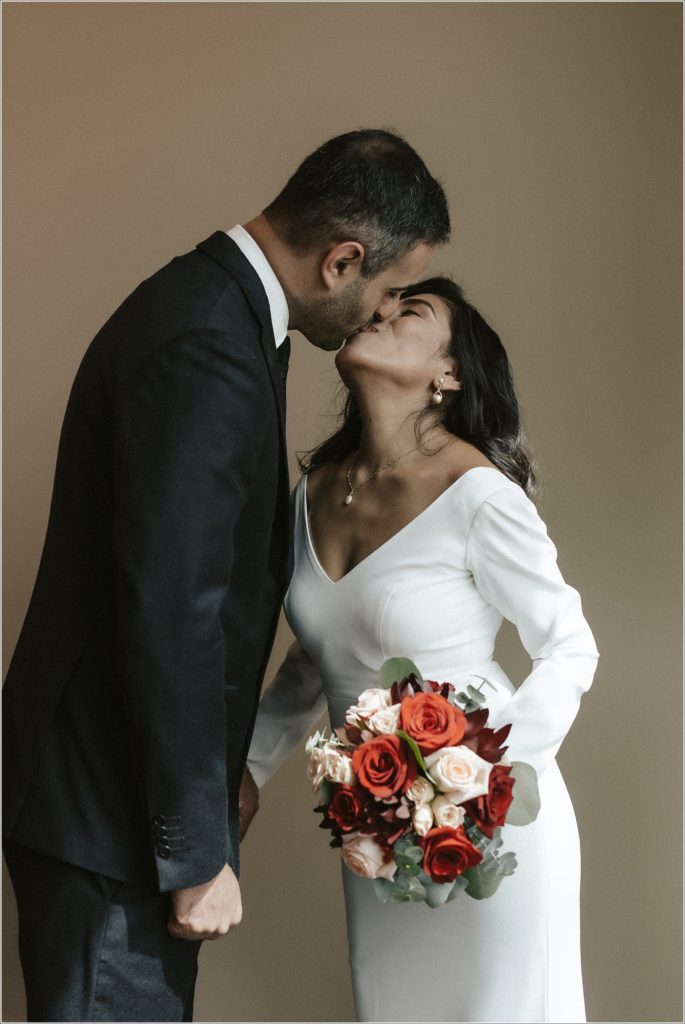 couple poses at courthouse wedding in maryland in white wedding dress and suit with red and pink bouquet