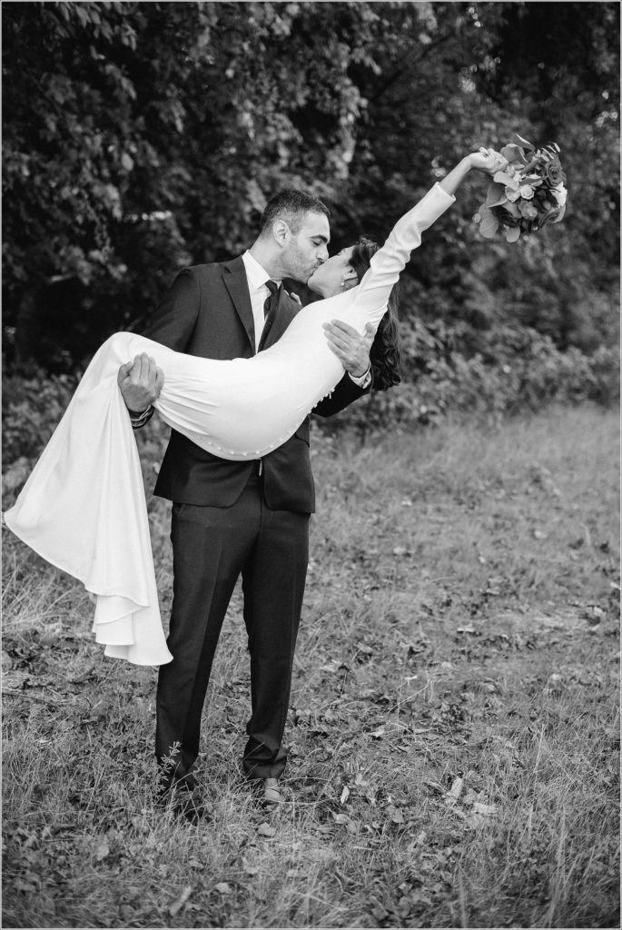 black and white photo of groom picking up bride as she tosses bouquet into the air