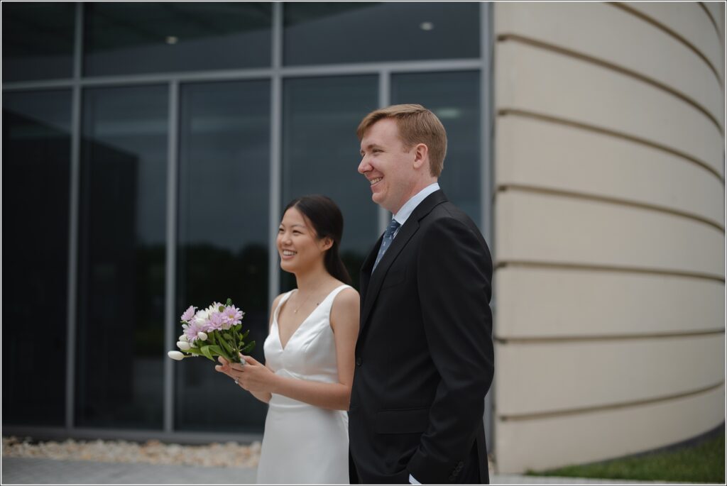 woman holding a purple bouquet and man in a black suit stand outside a Howard County courthouse wedding